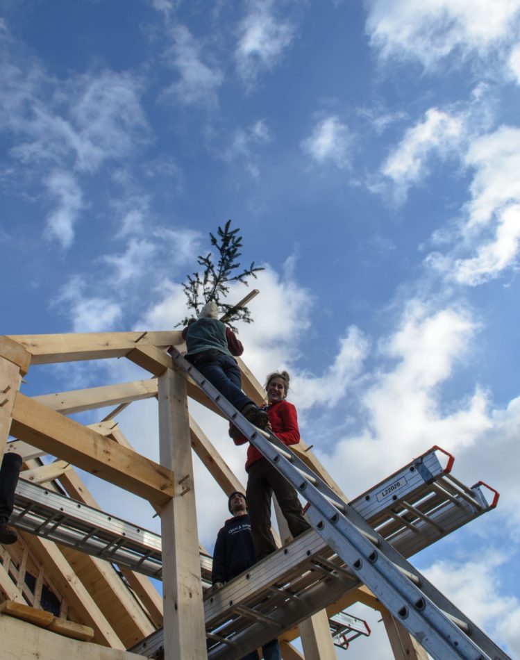 An evergreen branch is nailed to a new timber frame building