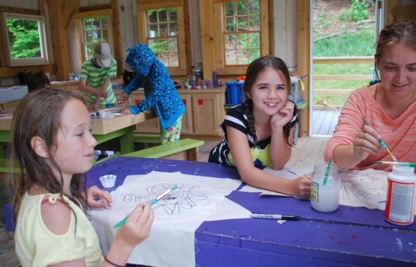Kids and their camp counsellor painting inside a post and beam barn