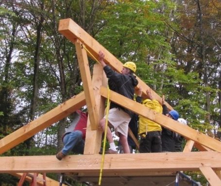 The ridge beam is lowered into position at a hand raising of a post and beam barn