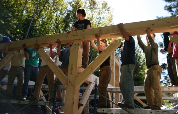 A group of people lower a beam onto a timber post and it's two braces