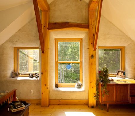 Plastered walls and bright sunlight make the bedroom of this timber frame house glow