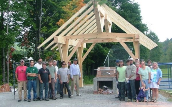 A group of volunteers gather in front of the bread oven and shelter they just built