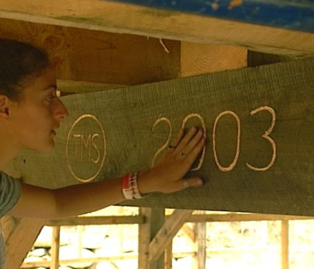 A student touches the engraving of the year 2003 in the tie beam of a timber frame barn