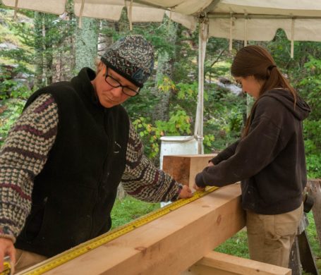 An instructor checks a student's work at a timber framing workshop in New Hampshire