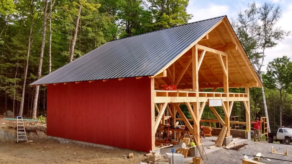 A timber frame barn with red shiplap siding and channel drain metal roof