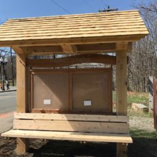 A timber frame kiosk with bench and display area and cedar shingle roof