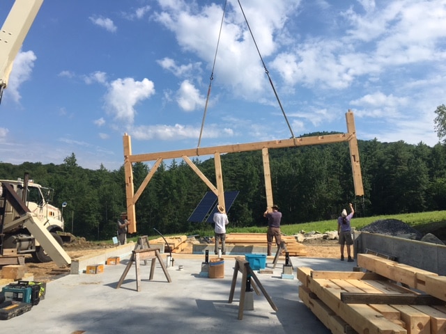 At a timber frame barn raising, a crane lowers the first bent into place