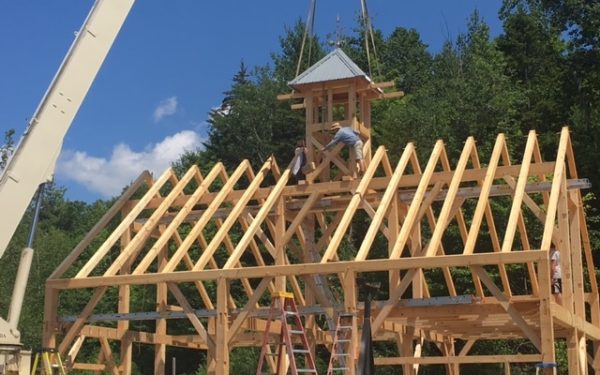 At a timber frame barn raising, the cupola is lowered into place with a crane