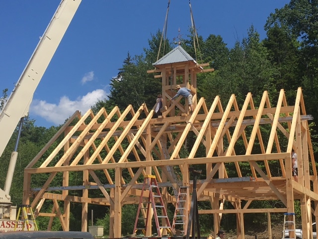 At a timber frame barn raising, the cupola is lowered into place with a crane