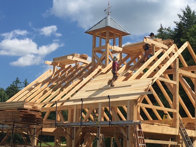 A timber frame barn with a cupola is beginning to be roofed