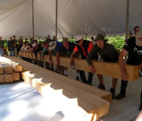 A dozen people carry a massive beam during a timber framing workshop