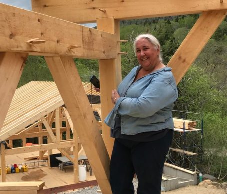 A workshop participant stands with a timber she cut in a finished timber frame