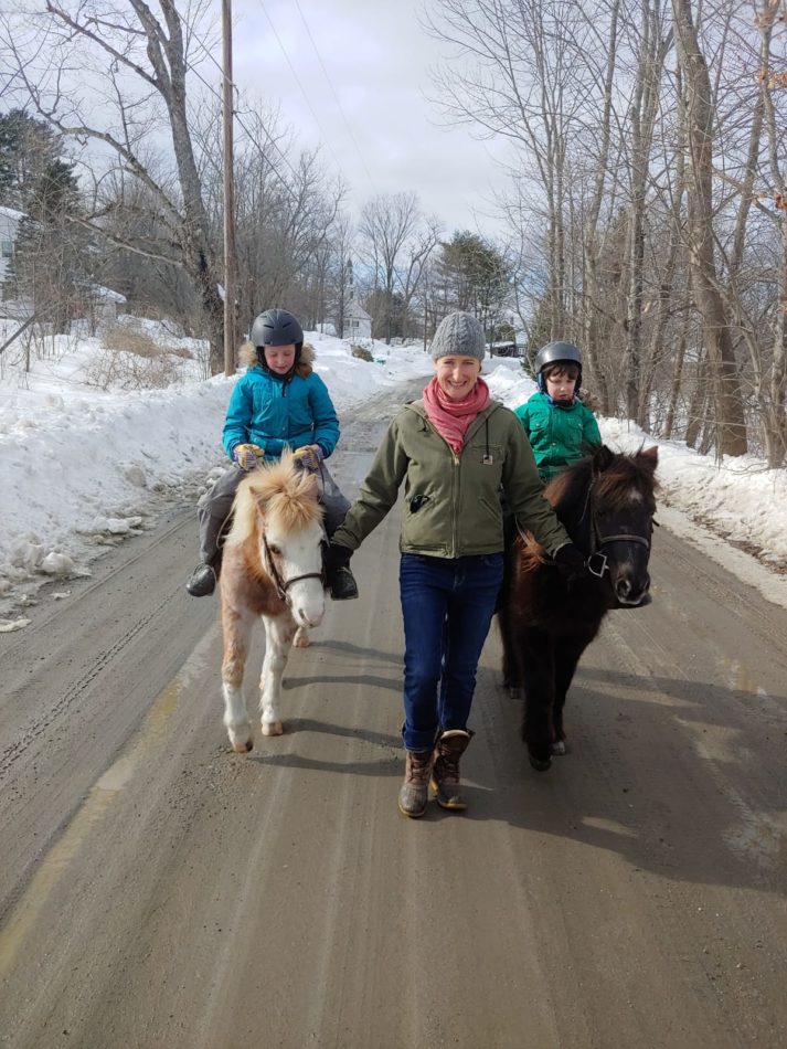 Rebecca Copans leads the two ponies that her daughters are riding down a dirt road in Vermont