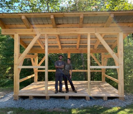 TimberHomes Vermont's Helen Doyle and Ben Schachner stand in the woodshed frame raised by family and friends of the client in Upstate New York