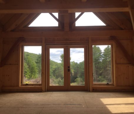 Looking out of the window wall of a timber frame cabin into the Vermont woods