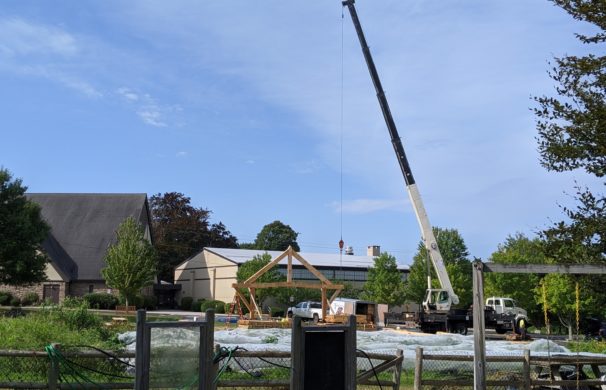 A crane raises a section of a timber framed pavilion to be used as an outdoor classroom in Massachusetts