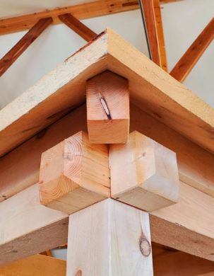 A close up detail of the joint between a post, two plates, and a hip rafter. the symetrical and angular geometry is fascinating