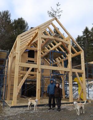 The two clients who commissioned this project, and their twin dogs, stand happily in fron of their freshly raised timber frame