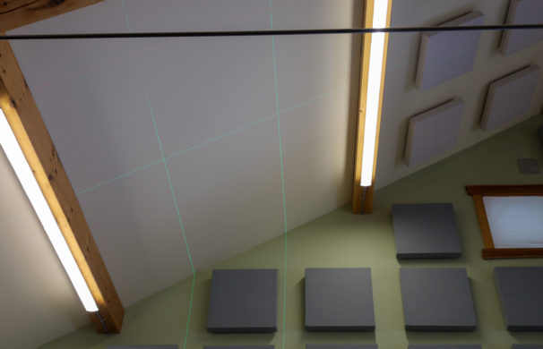 Laser lines projected onto a ceiling in a timber frame woodshop where sound dampening panels are being installed