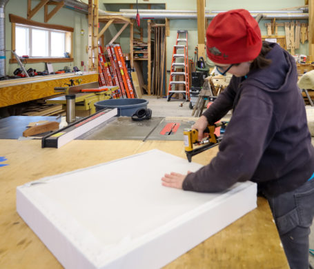 A craftsperson upholsters fabric over a wooden frame stuffed with wool insulation to create a sound dampening panel