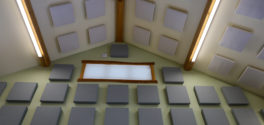 An upward facing image of sound dampening panels hung amidst a timber frame woodshop ceiling and walls