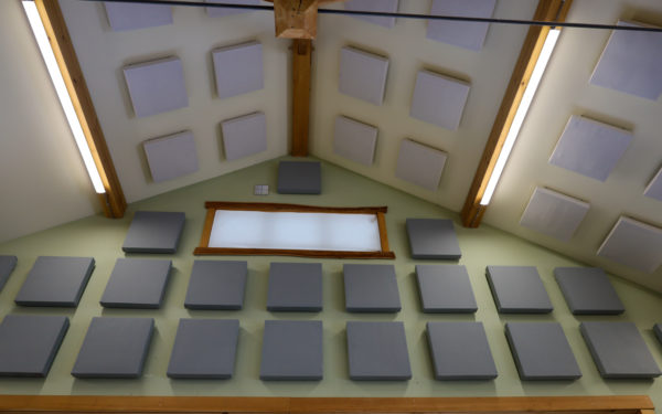 An upward facing image of sound dampening panels hung amidst a timber frame woodshop ceiling and walls