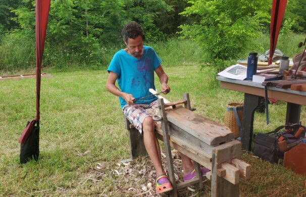 A person makes wood pegs by drawknifing them on a shave horse