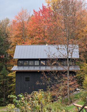 A black timber frame barn on a hillside with Fall colors.