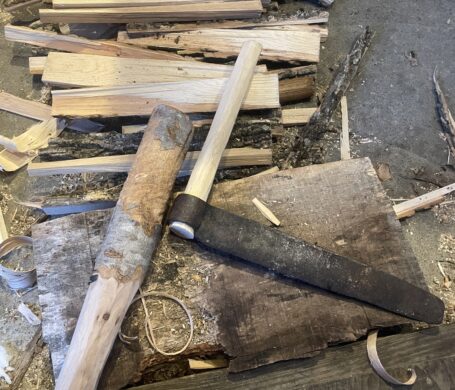 A pile of wooden rods that have been riven into rectangles, and a tool called a froe, used for splitting wood.