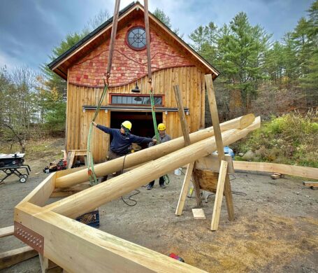 Two round log rafters are being installed into a 10-sided roof.