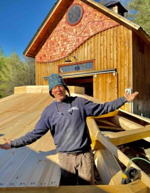 Timber Frame designer Josh Jackson stands in a space between rafters of a reciprocating roof.