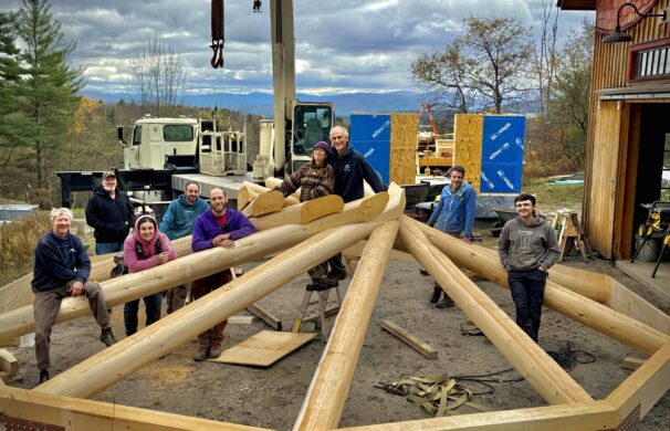 A group of people pose intermingled with the rafters of a reciprocating roof.